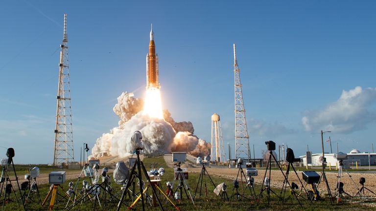 NASA's Space Launch System rocket carrying the Orion spacecraft lifts off for Artemis II, with cameras set up in the foreground and launch towers framing the scene.